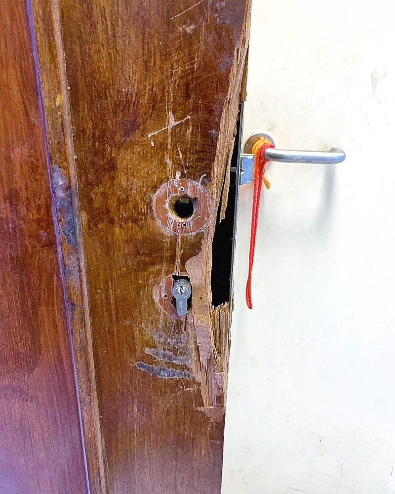 Damaged wooden HDB main door with the old lock removed and a splintered edge